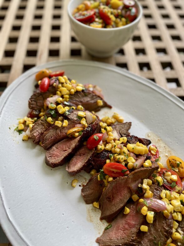 a flat iron steak recipe cooked and sliced on a white platter with corn salsa on top