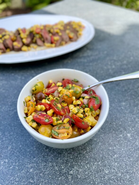 a bowl of corn salsa with flat iron steak on a platter in the background