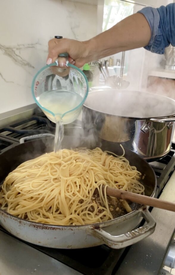 adding pasta water to the skillet of pasta