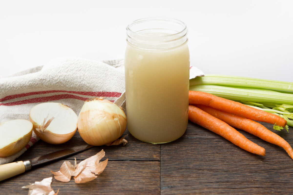 Golden homemade chicken stock cooling in glass jars on the counter