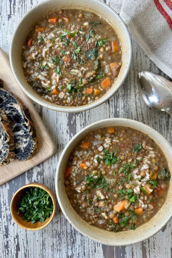 two bowls of lentil and brown rice soup with bread and herbs