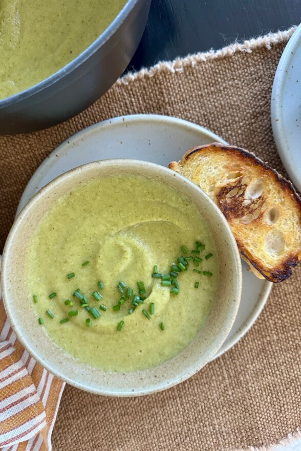 finished bowl of broccoli soup with bread on the right, big bowl in the back