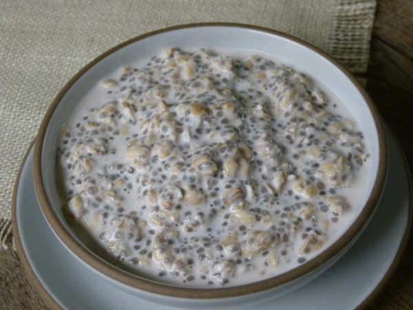 Side view of a white bowl of overnight chia oat porridge, showing thick creamy texture with visible chia seeds and fruit.