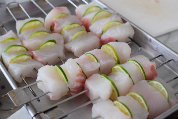 Close-up of fresh halibut and lime slices threaded onto skewers before grilling.