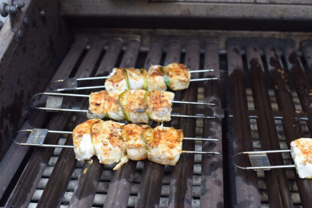 Halibut skewers grilling on a barbecue with visible char and golden edges.