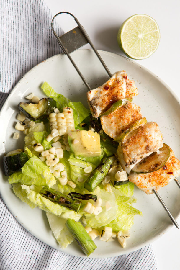 Plated halibut skewers served with lime wedges and herbs, styled for summer dinner.