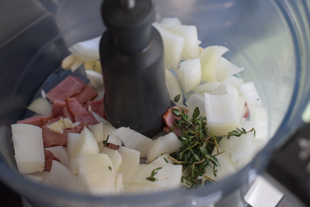 Turkey meatloaf recipe ingredients including onion, turkey bacon, and fresh thyme in a food processor ready to combine.