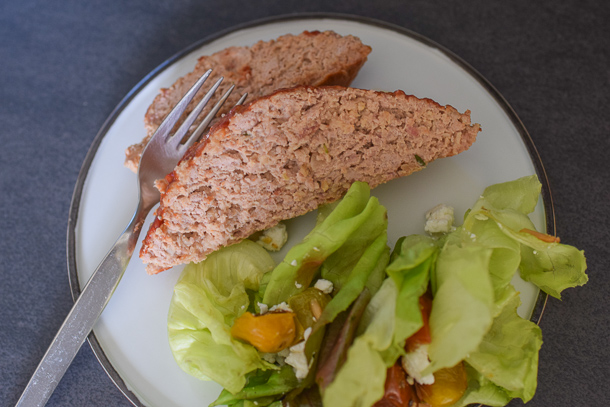 Thick slices of juicy turkey meatloaf plated and ready to serve, garnished with herbs and accompanied by green beans and roasted vegetables.