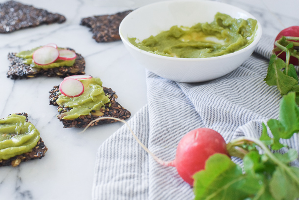 a seed cracker topped with avocado spread