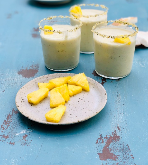 pineapple wedges on a plate next to smoothies in short glasses