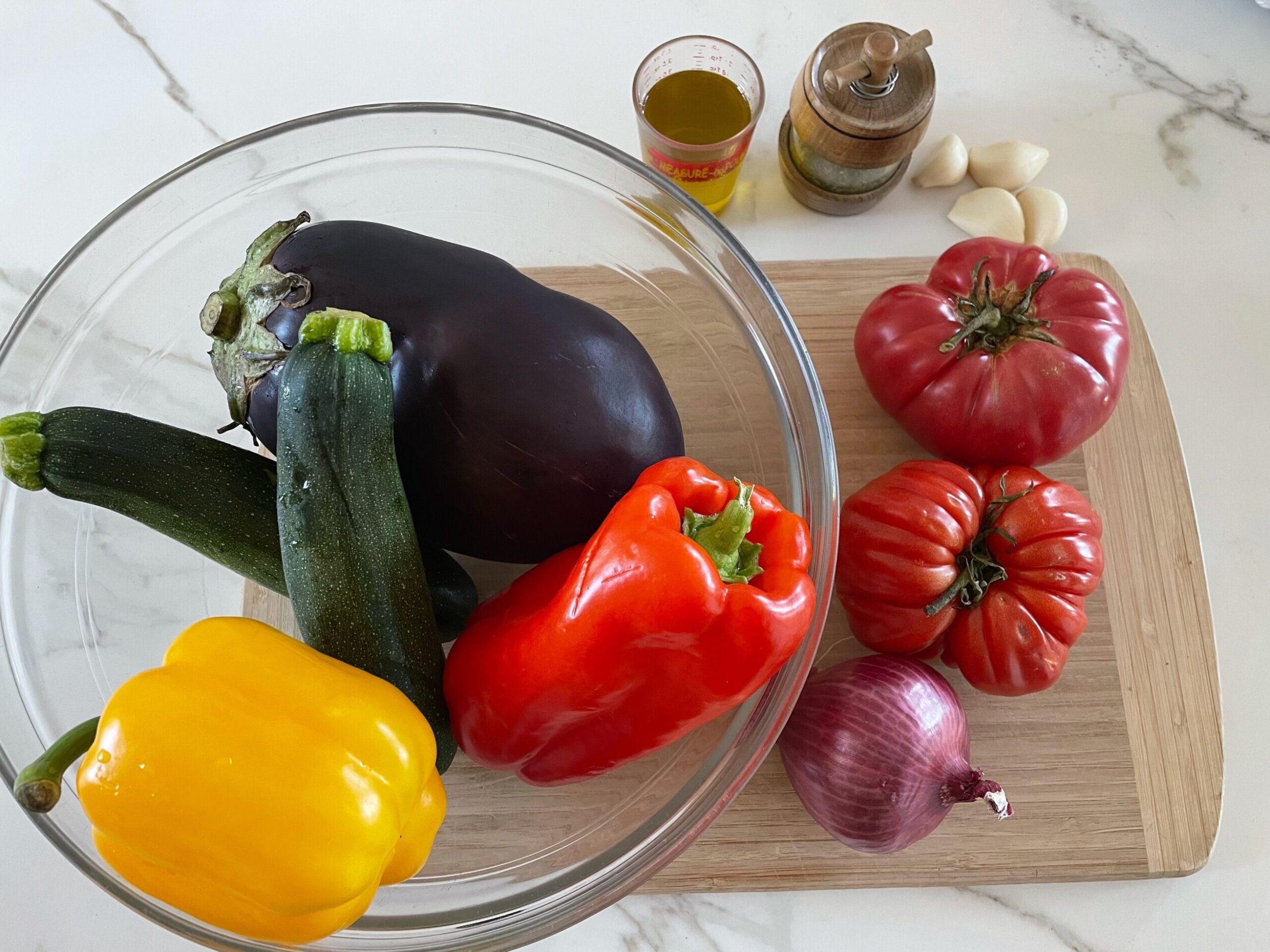 Raw ingredients for ratatouille including eggplant, zucchini, bell peppers, and onion on a cutting board.
