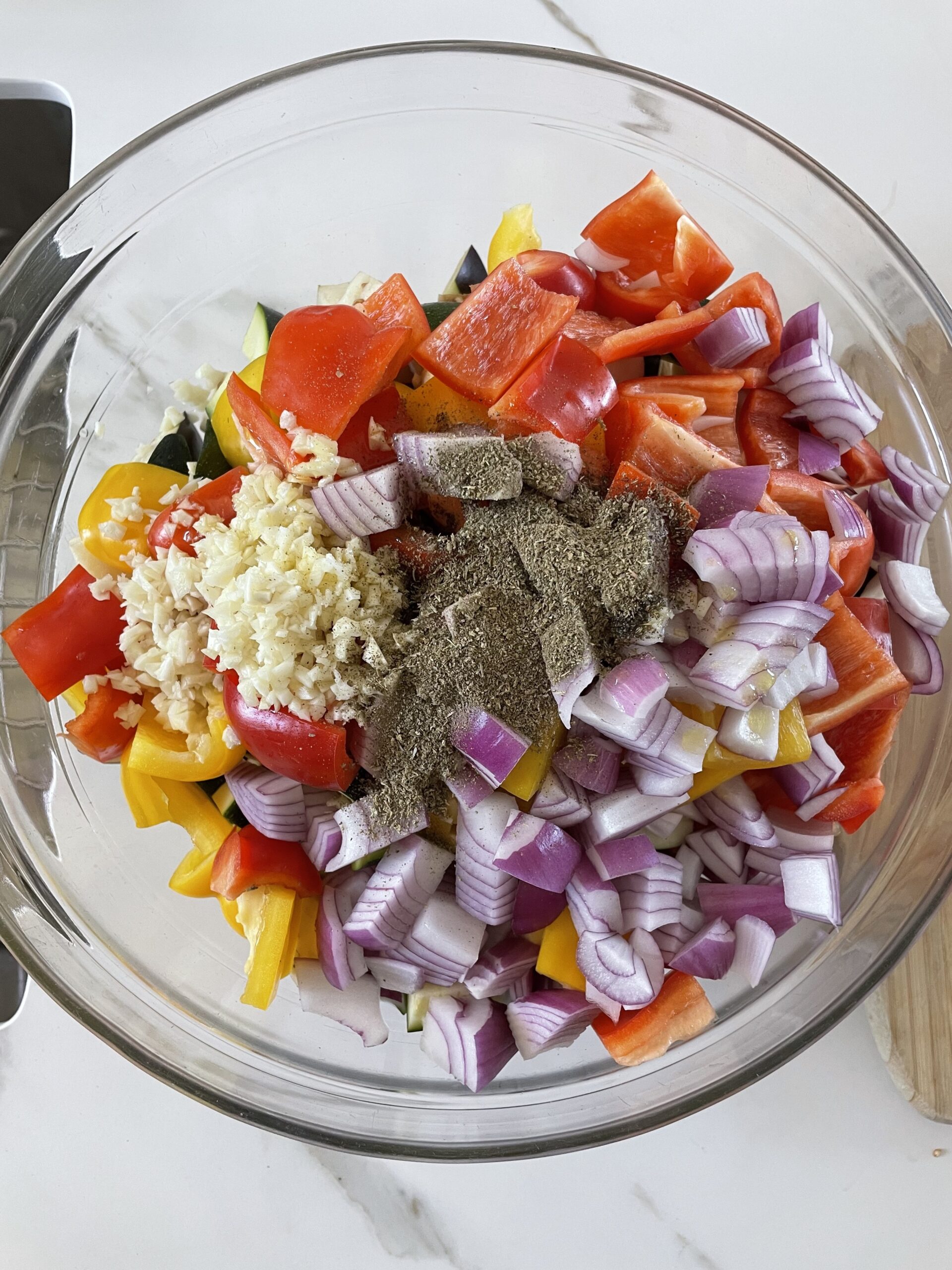 Chopped vegetables tossed with oil and herbs in a mixing bowl, ready for roasting.