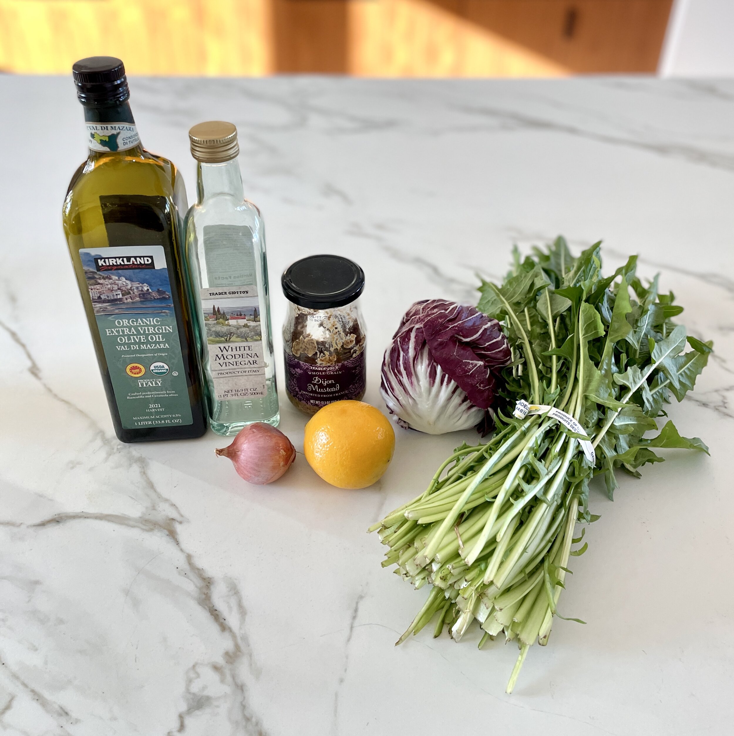 Ingredients for dandelion salad arranged on a countertop, including dandelion greens, radicchio, Meyer lemon, shallot, and white balsamic vinegar.
