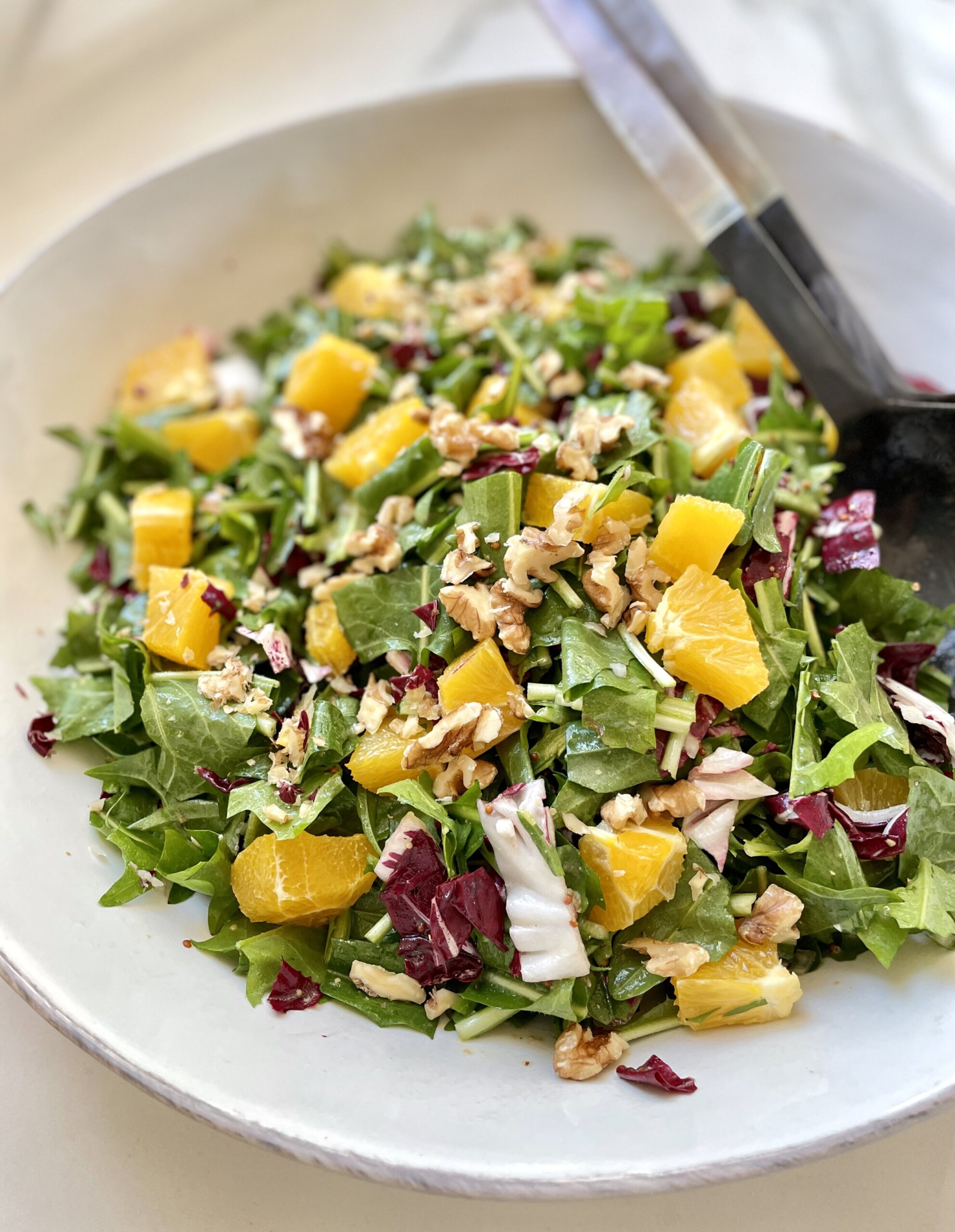 Finished dandelion salad plated in a shallow serving bowl, topped with walnuts, herbs, oranges, and vinaigrette.
