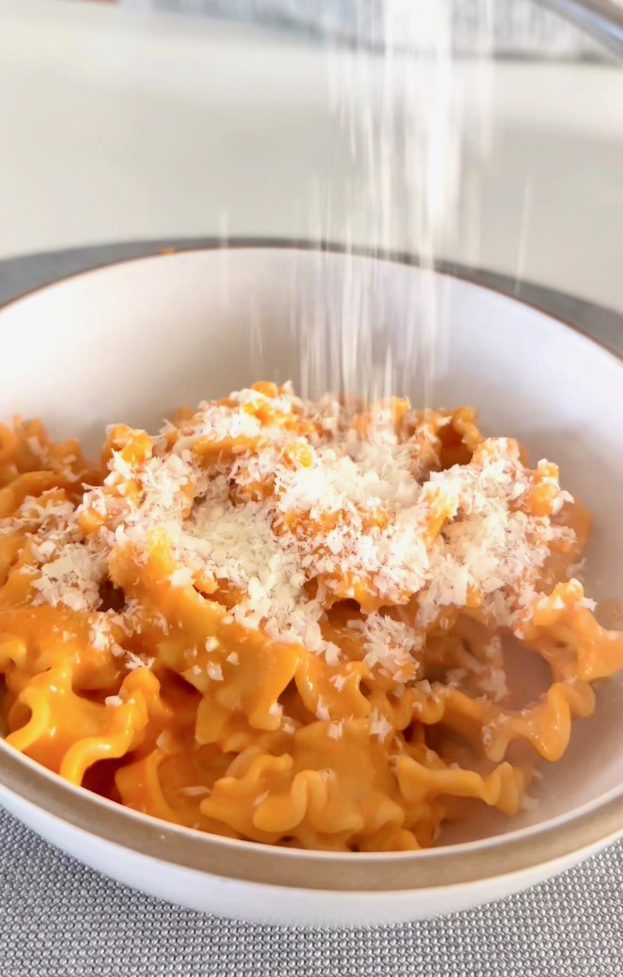 Finished vodka pasta served in a bowl with Parmesan and fresh basil garnish