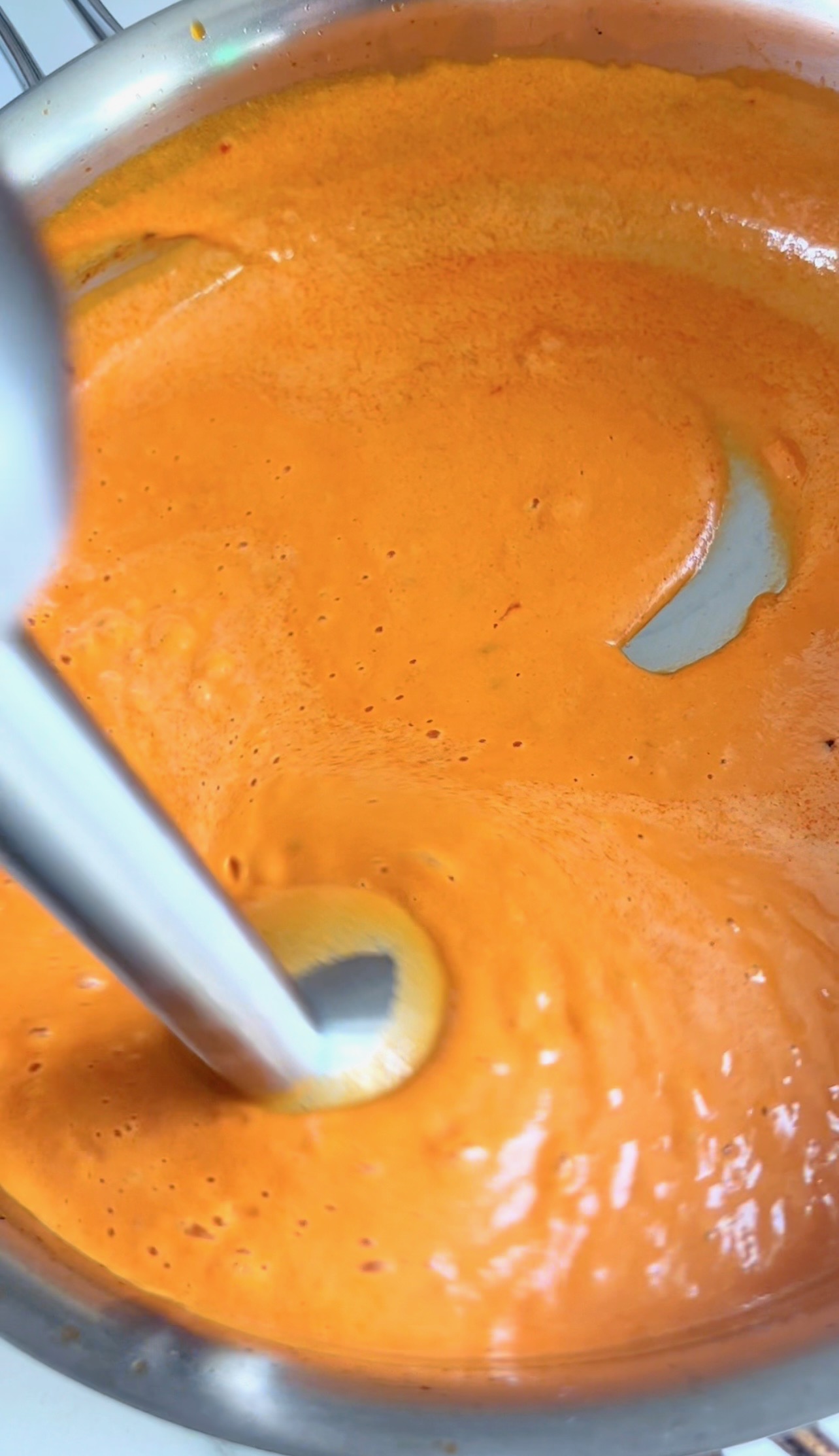 Pouring vodka into the tomato cream sauce to balance and emulsify.