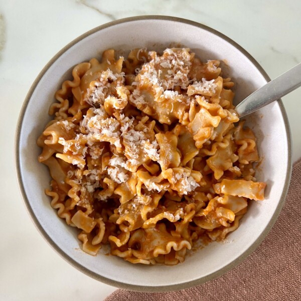 vodka pasta recipe in a white bowl with a fork and topped with parmesan cheese