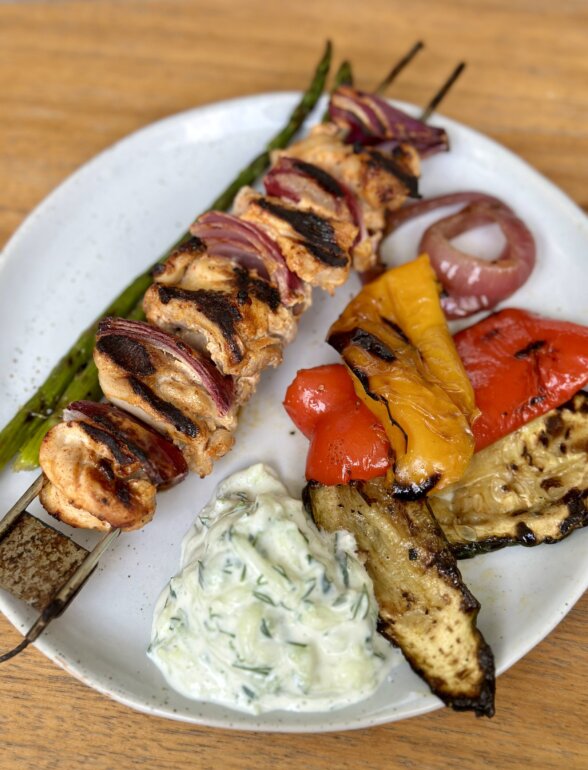 a yogurt marinated chicken skewer on a plate with veggies and tzatziki