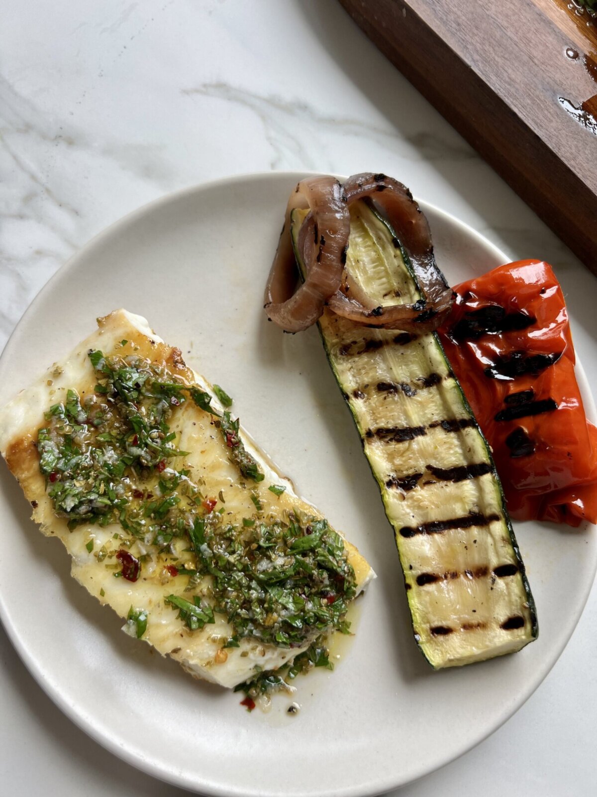 fish with salmoriglio sauce next to roasted veggies on a white plate