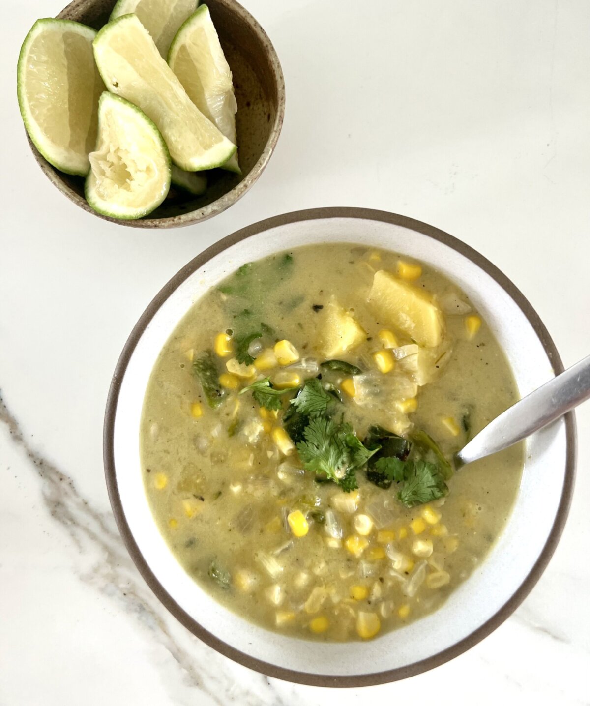 a bowl of poblano soup next to a small bowl of lime wedges