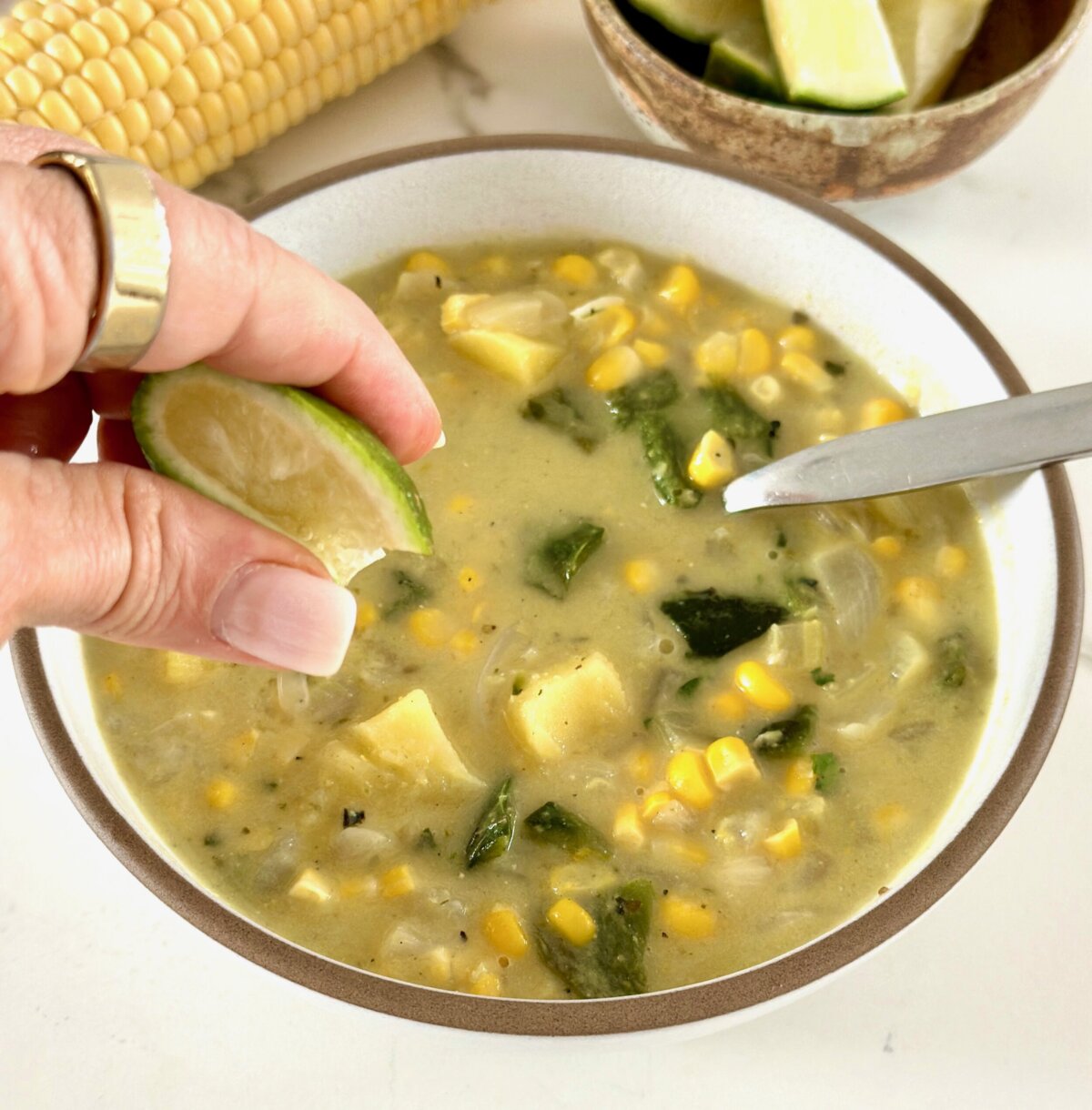 a hand squeezing a lime into a bowl of roasted poblano soup