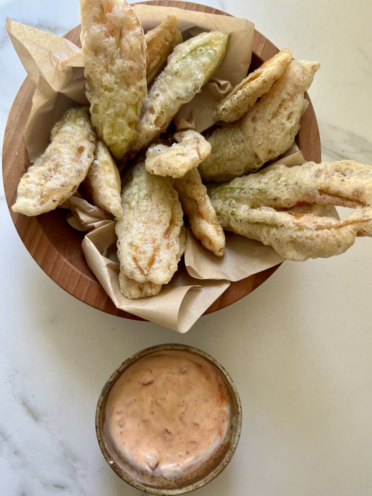 fried zucchini flowers in a bowl next to dipping sauce