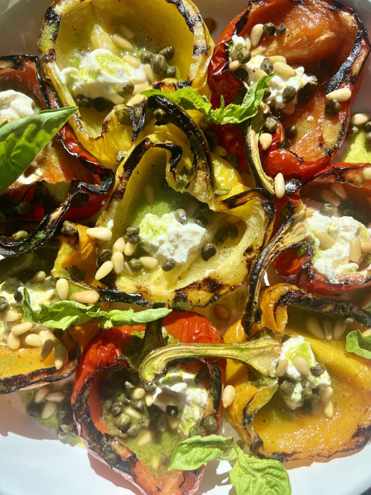 a close up shot of peppers stuffed with burrata and topped with pine nuts and basil