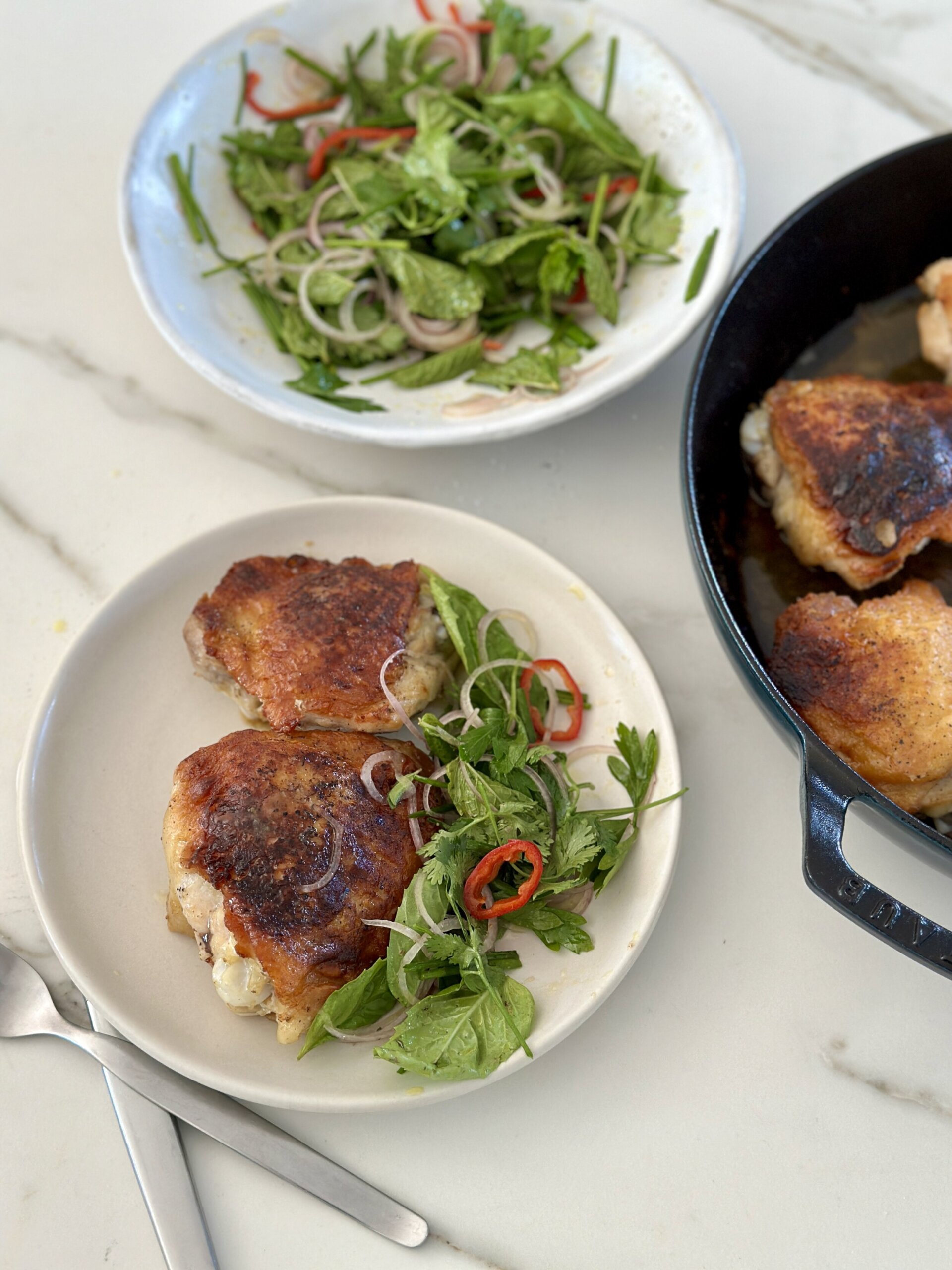 chicken in skillet and on a plate next to an herb salad