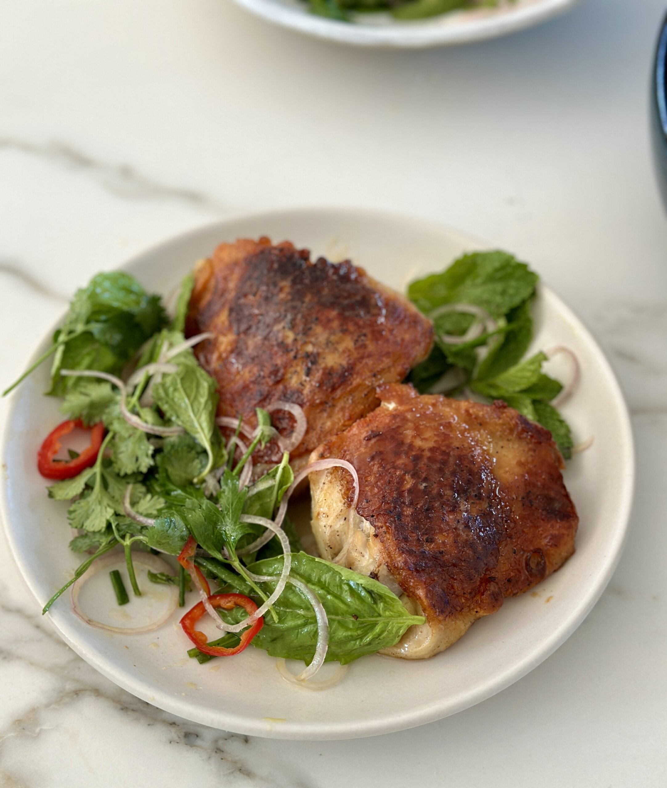 chicken thighs and herb salad on a white plate