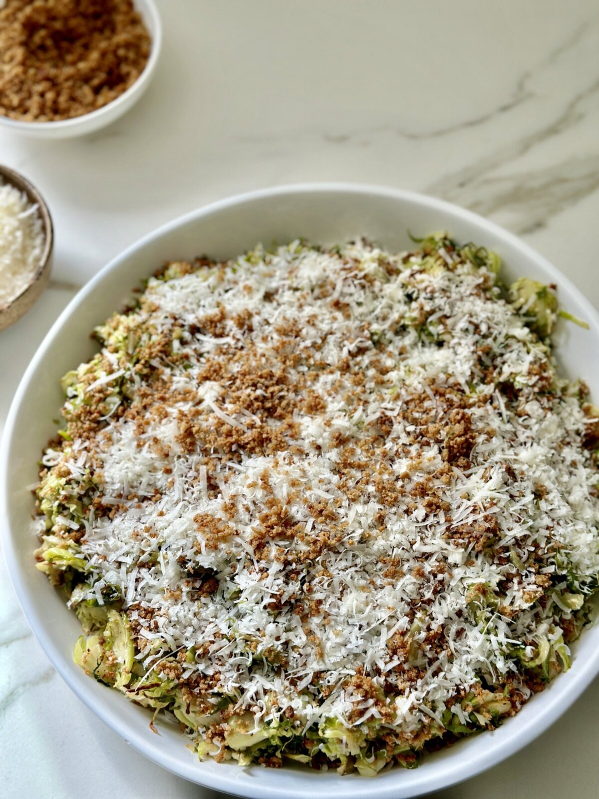 a brussels sprouts caesar salad in a white bowl topped with toasted breadcrumbs and parmesan cheese