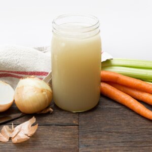 chicken stock by carrots, celery, and onions sitting on a table