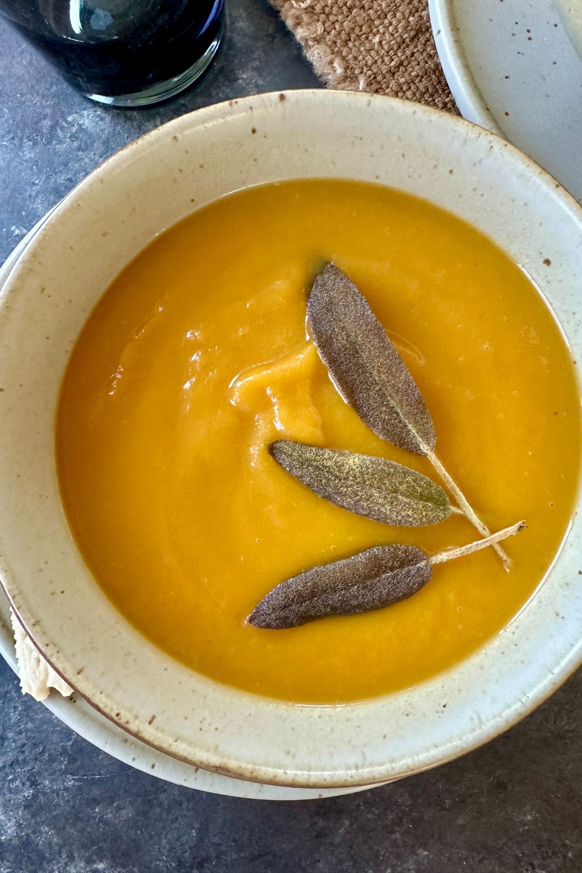 a bowl of butternut squash and apple soup topped with sage