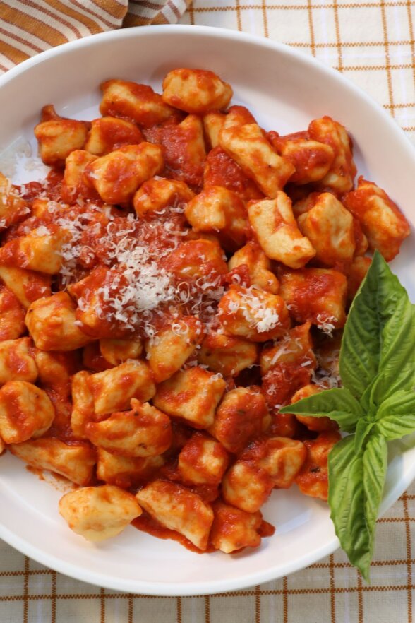 mashed potato gnocchi on a white plate with sauce and basil