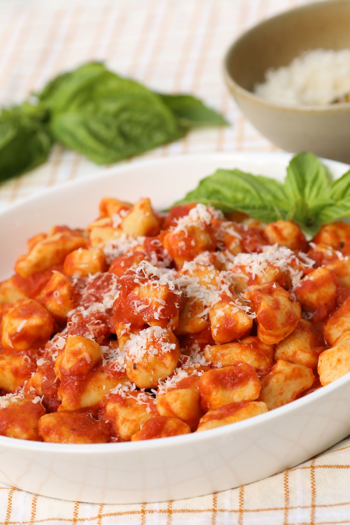 mashed potato gnocchi in a white serving bowl with sauce and basil