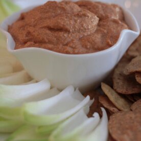 Bowl of Muhammara dip served with chips and celery