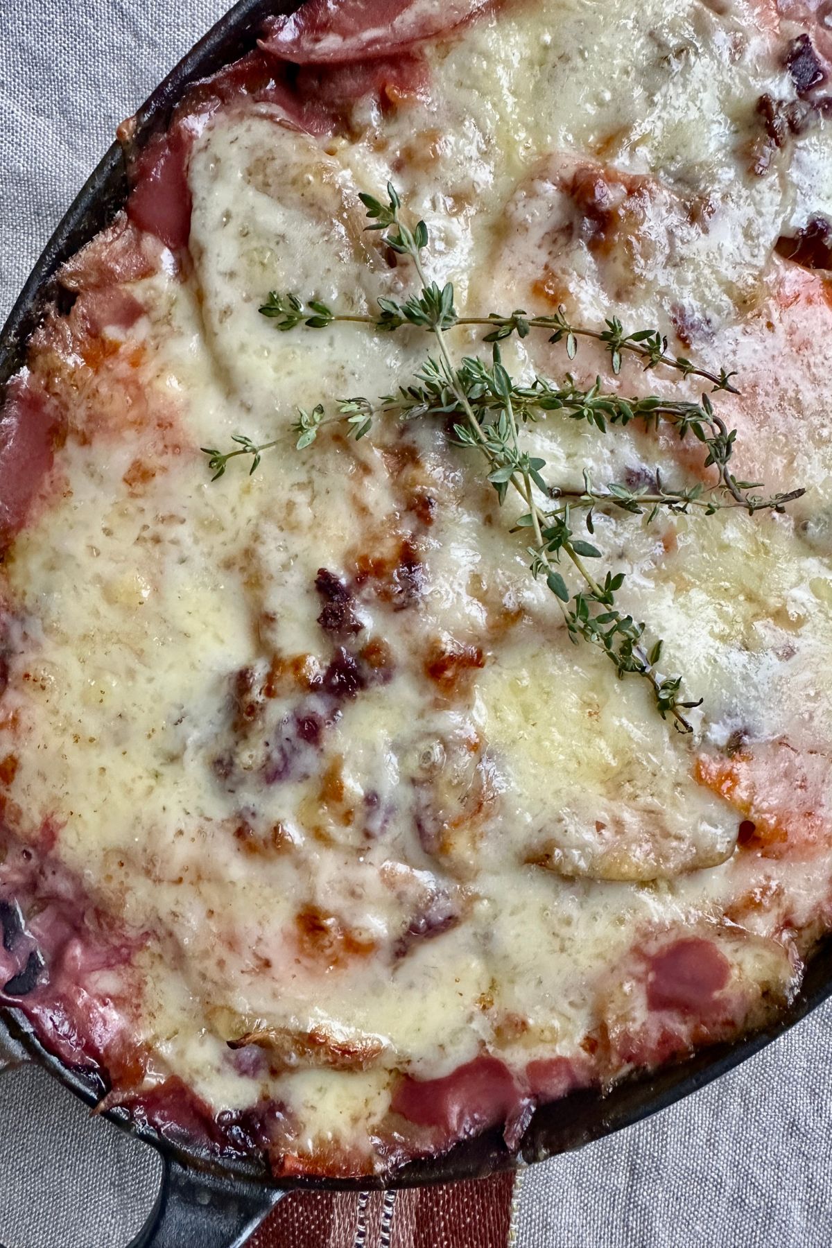 showing a close up of fresh thyme resting atop a cheesy root vegetable gratin