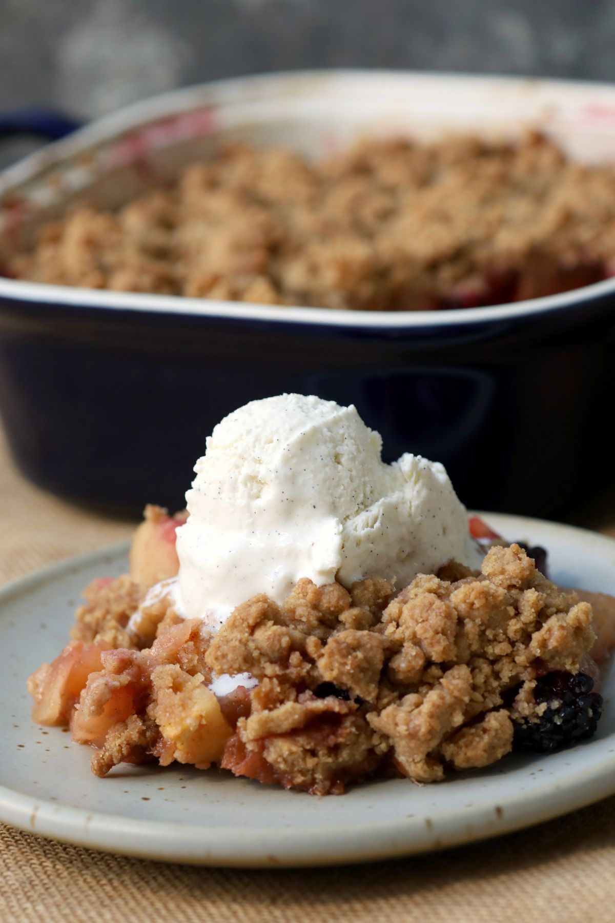 a serving of apple blackberry crumble on a plate topped with ice cream