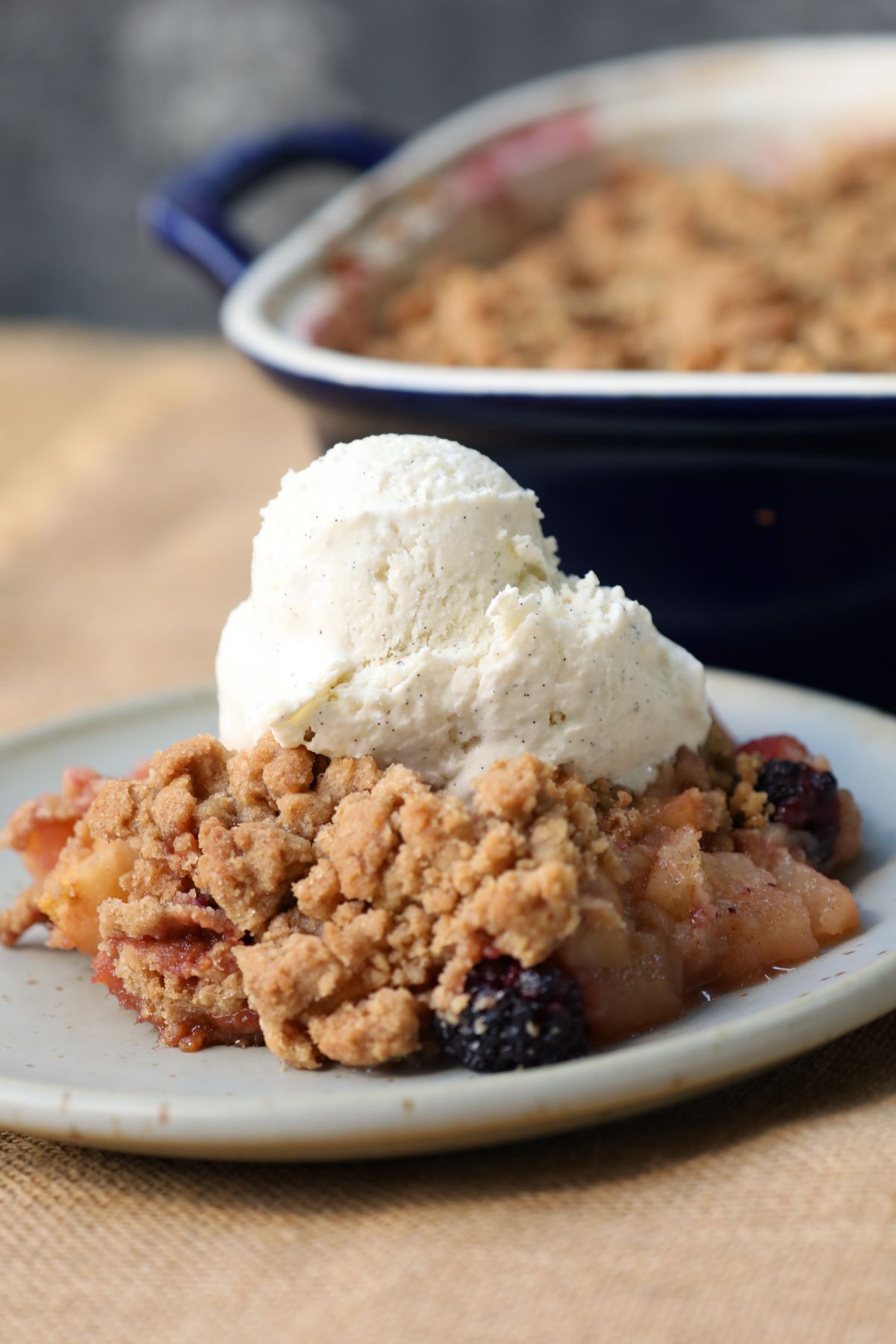 apple blackberry crumble on a plate topped with vanilla ice cream