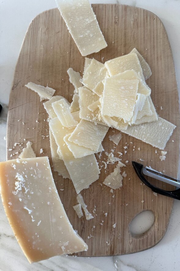 block of parmesan cheese flakes on wooden cutting board