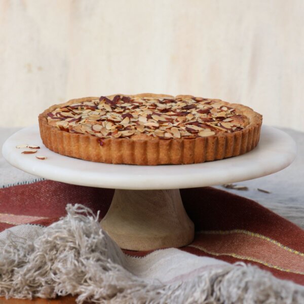 cherry bakewell tart on a white cake stand