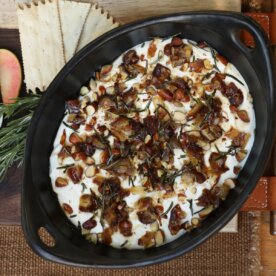 whipped goat cheese dip in a serving dish topped with dates, rosemary, and shallots