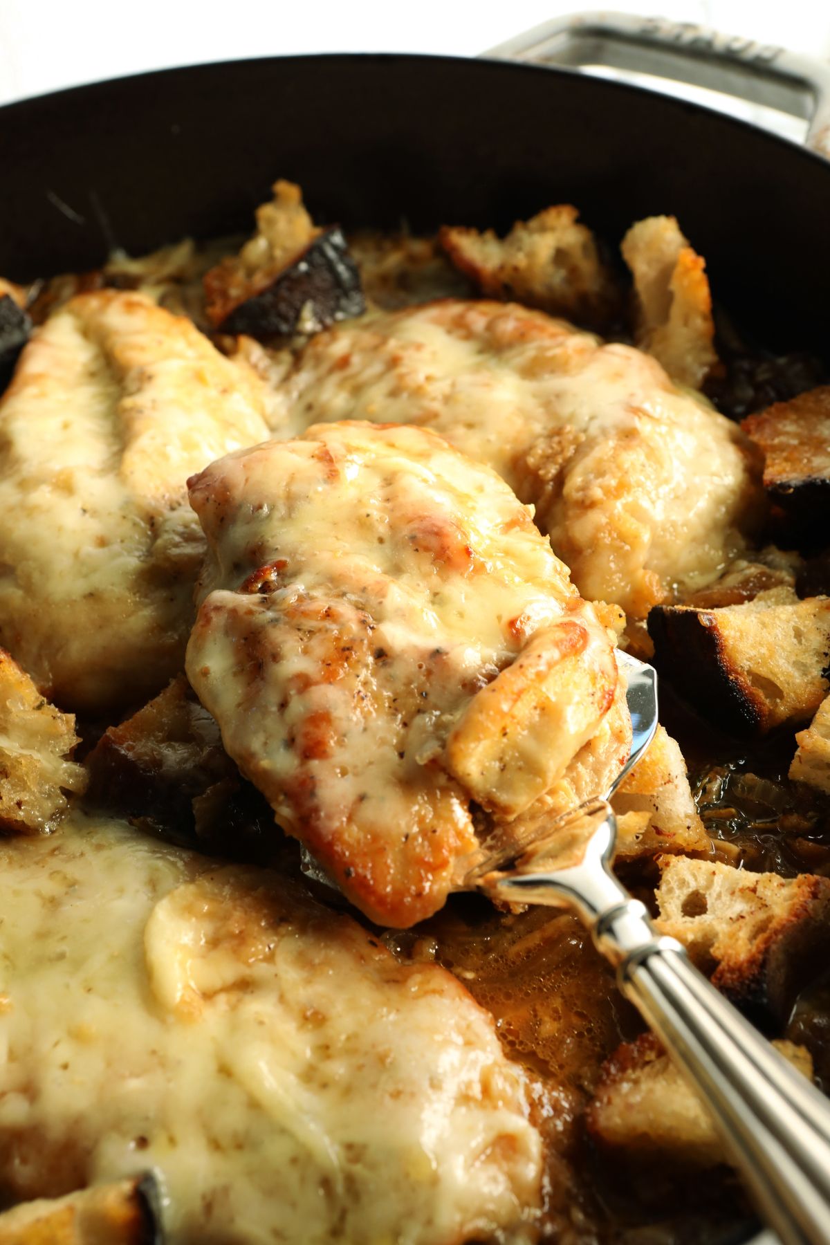 lifting chicken out of a skillet with a metal spoon