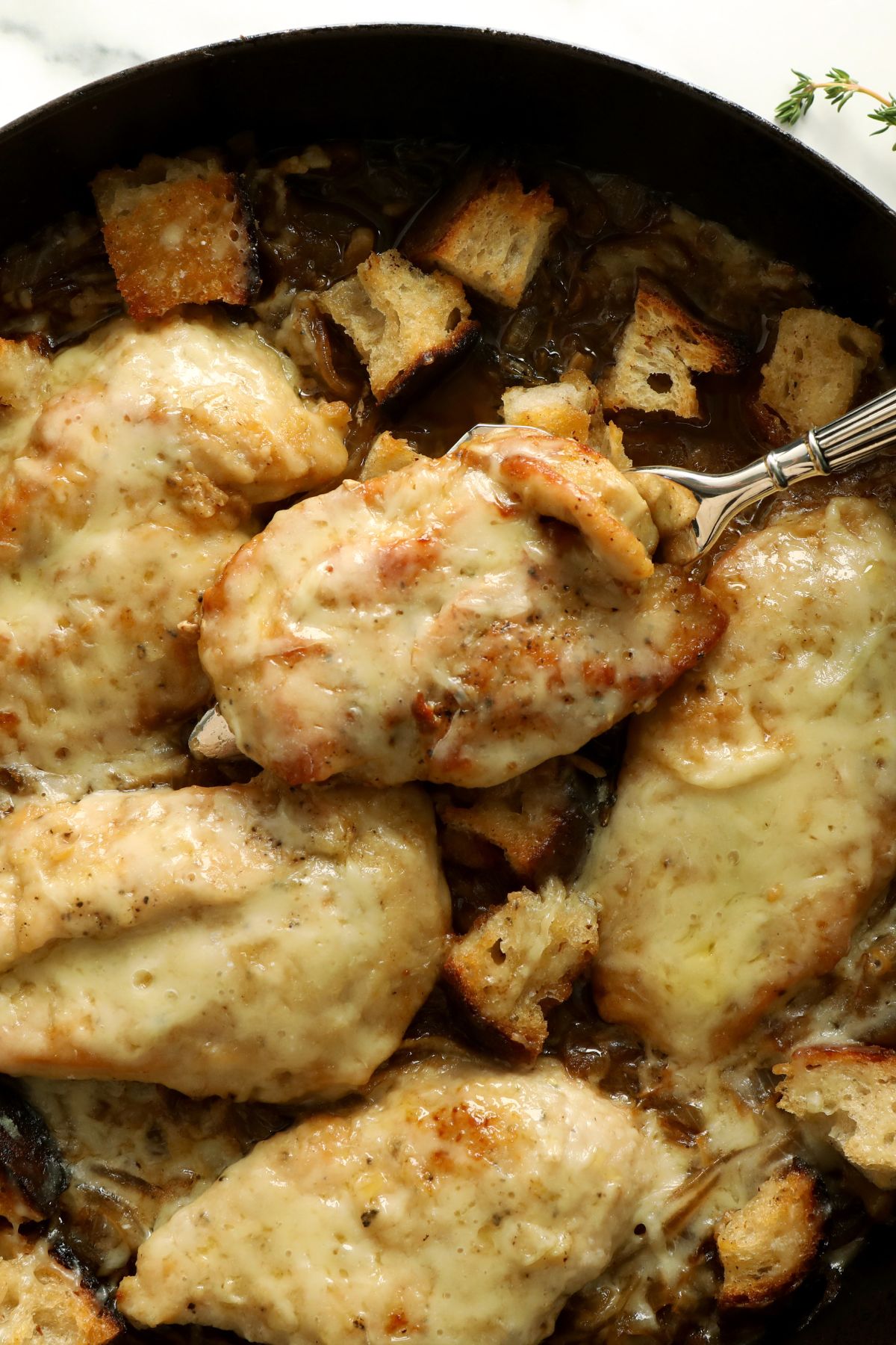 lifting chicken out of a skillet with a metal spoon