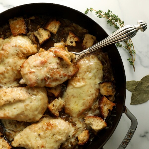 a spoon lifting a piece of french onion soup chicken out of a skillet