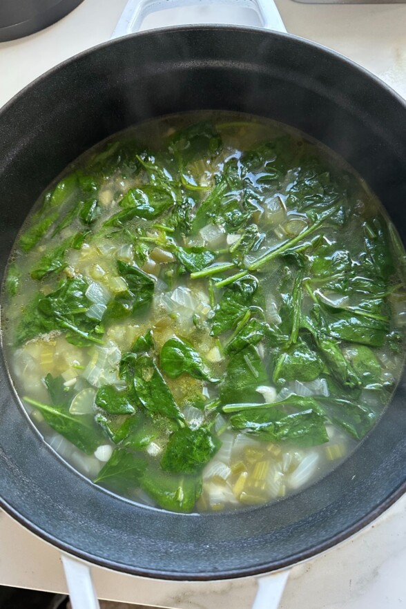 wilted spinach added to the pot with the broth and veggies