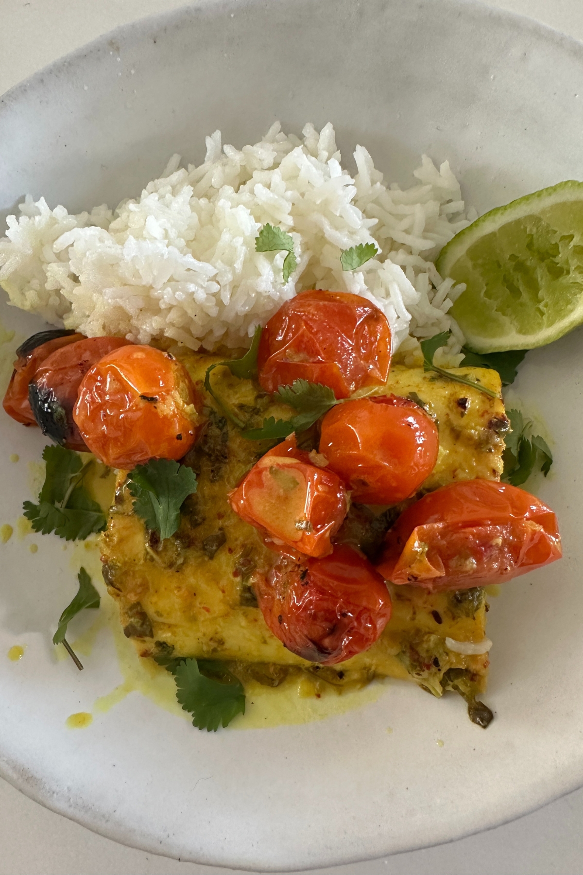 a serving of fish and tomatoes atop rice with a lime wedge 