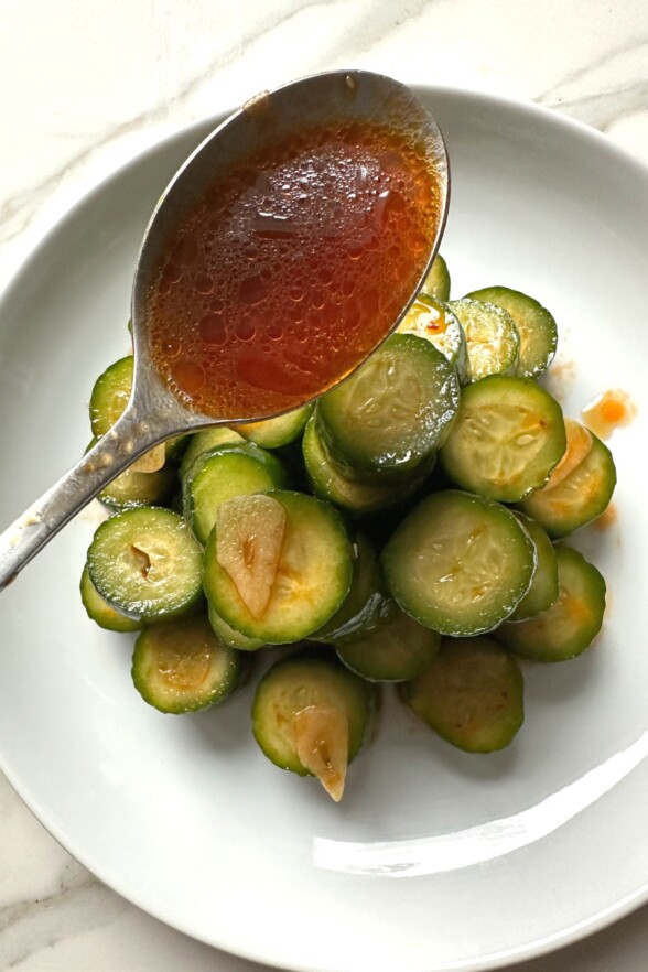 A spoon drizzling extra spicy dressing over the cucumber salad for added flavor.