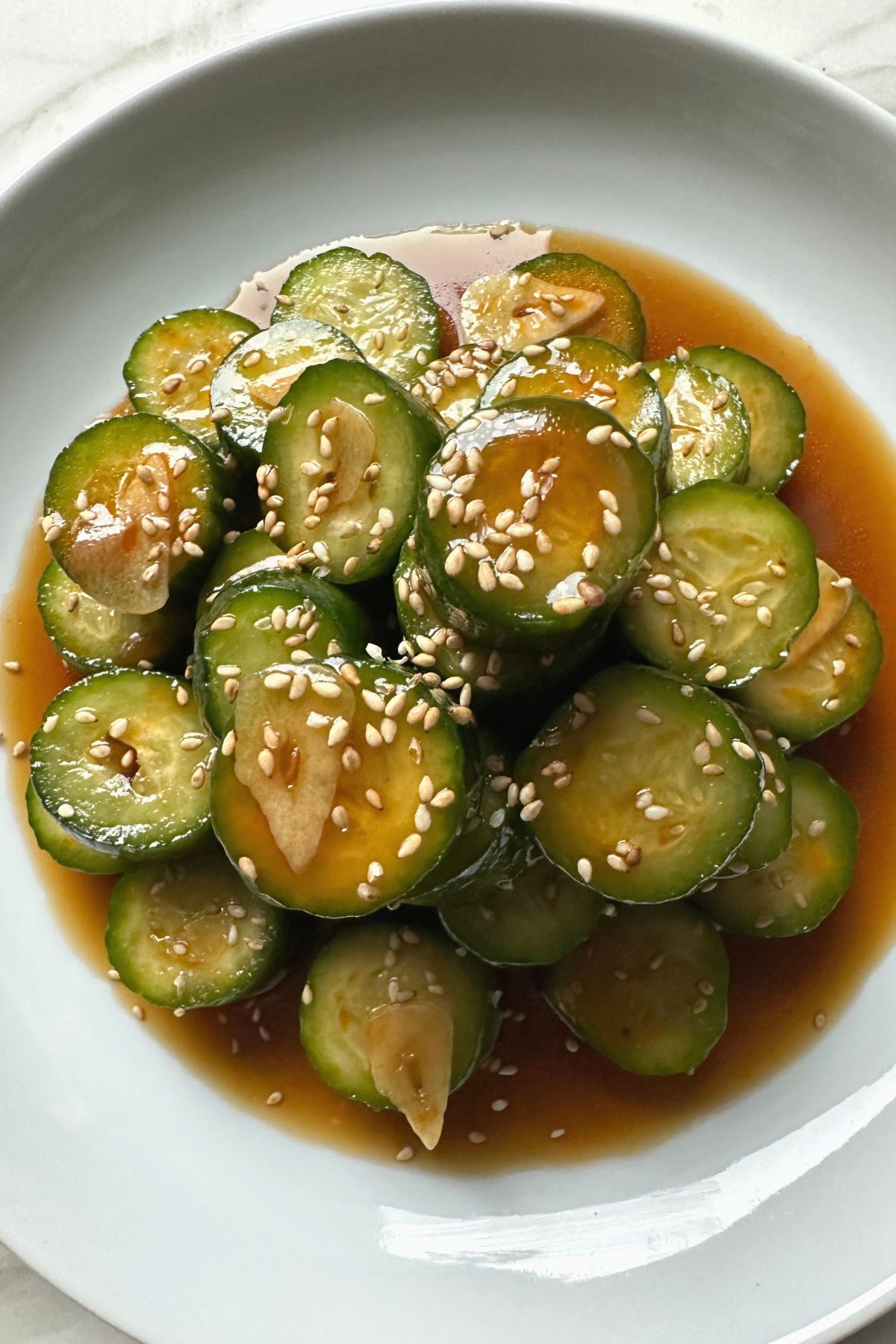 Spicy cucumber salad served in a white bowl with chili oil drizzle and garlic slices
