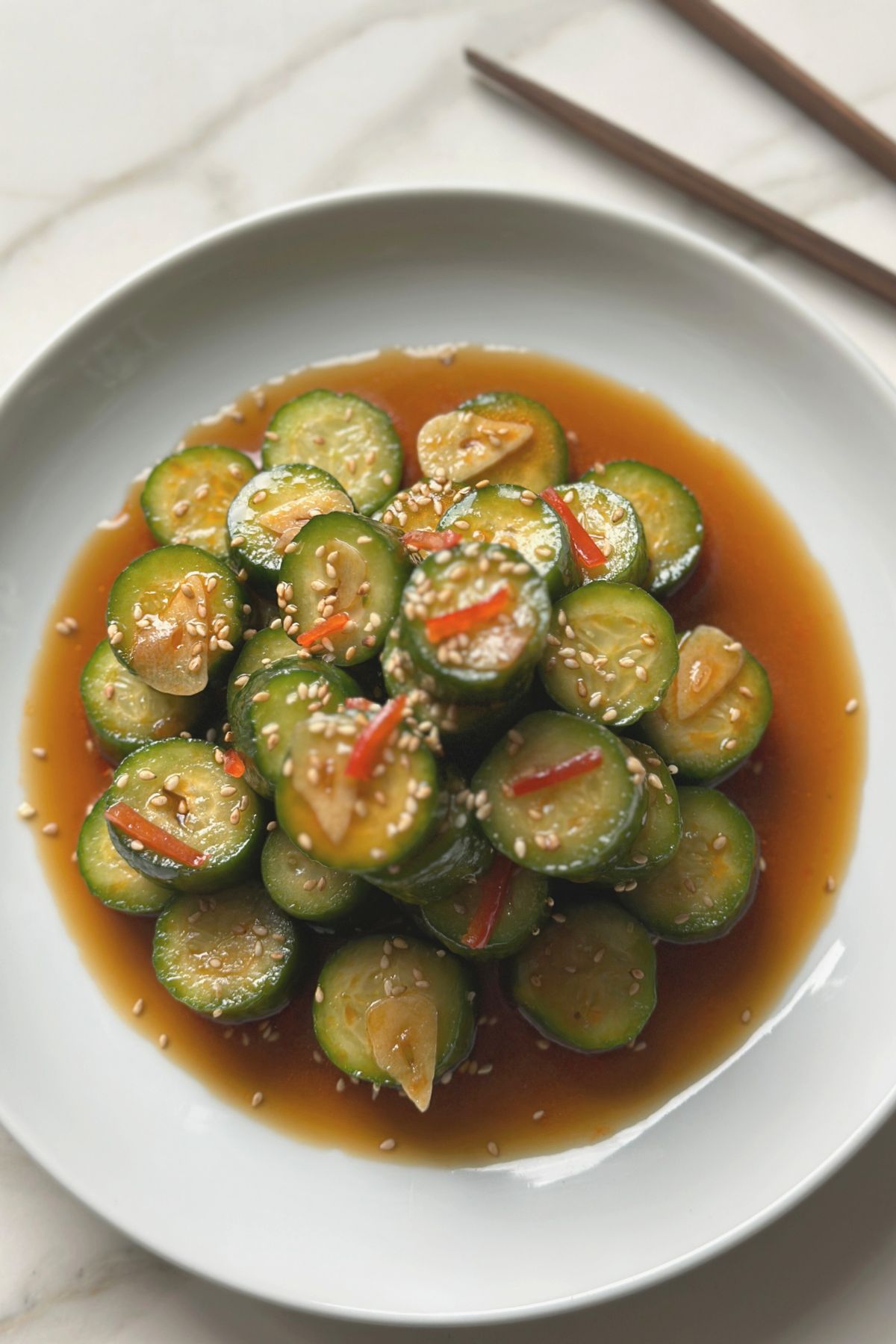 plated spicy cucumber salad garnished with red pepper slices and sesame seeds on a white plate. 
