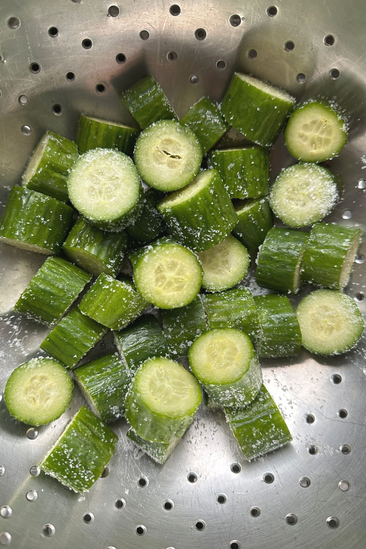 Cucumber slices being salted in a colander to remove excess moisture
